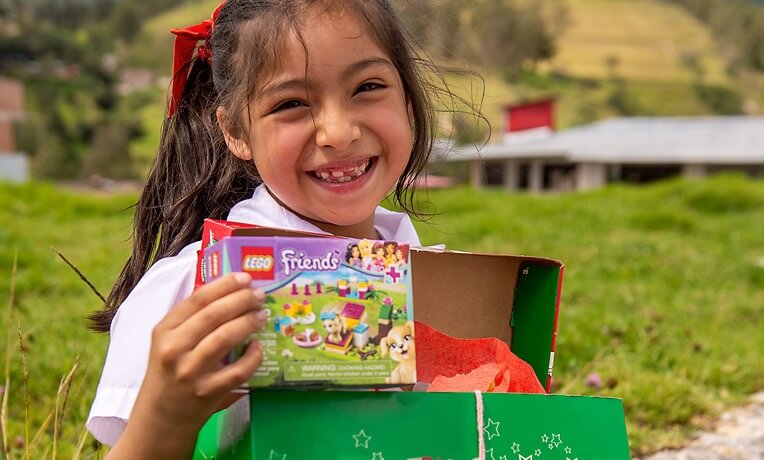 A smiling girl holds up a toy from her Operation Christmas Child shoebox gift